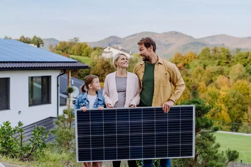 Iloinen perhe pitämässä kädessään aurinkopaneelia ja kaunis maisema.